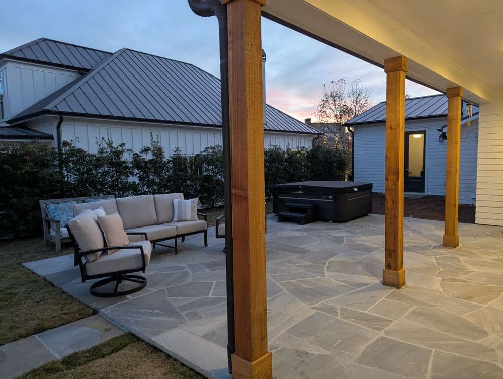 Patio with stone floor, wooden pillars, seating area, and hot tub at sunset.