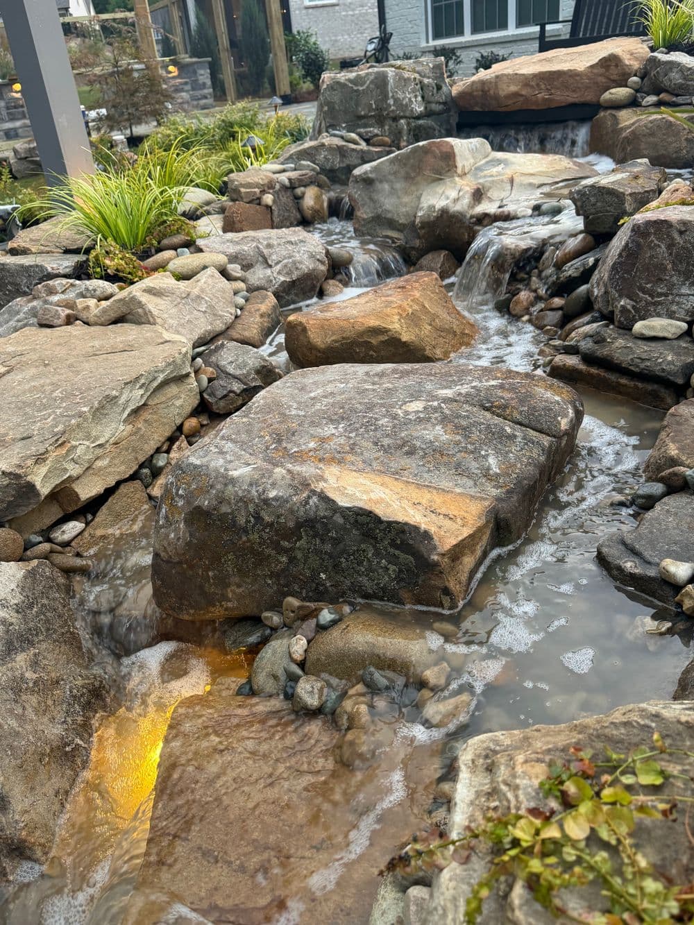 Natural stone water feature with flowing streams and lush greenery in a landscaped garden.