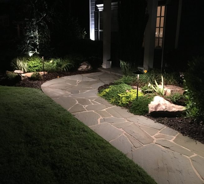 A lit pathway leading to a front door. Outdoor lighting installed by StoneAge Stonescapes